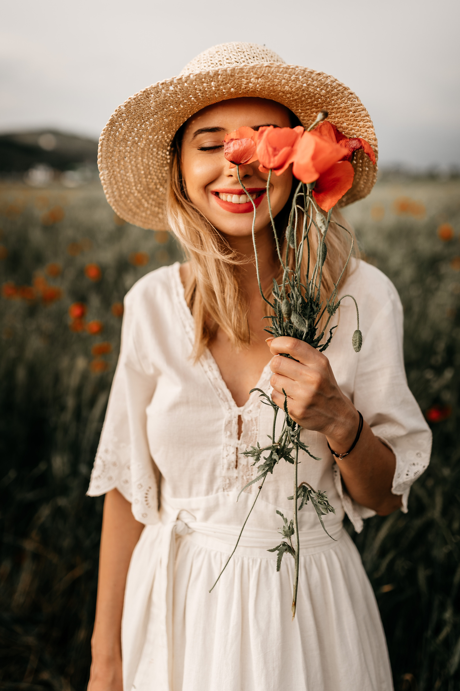 Charming woman in hat with flowers in meadow